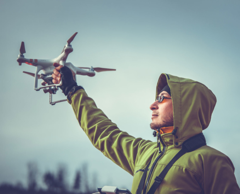Drohnenversicherung: Ein Mann mit grüner Kapuzenjacke hält seine versicherte Drohne in der Hand.