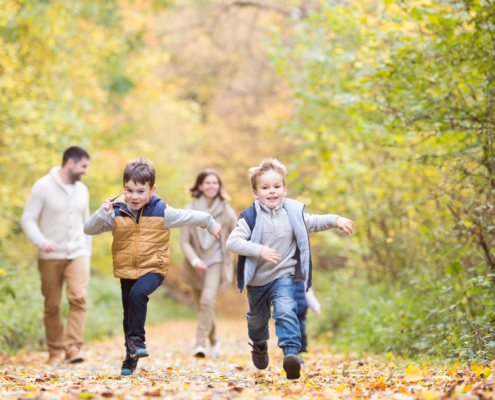 Angehörigen Schutz bei Todesfall: Junge Familie mit zwei Söhnen spazieren im Wald. Die Kinder rennen. Die Familie hat eine Versicherung für Angehörige bei Todesfall.