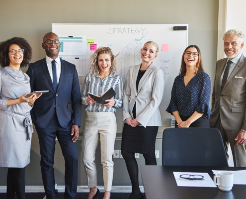 Für Unternehmen: Team eines Unternehmens posieren vor der Strategietafel und lächeln glücklich.